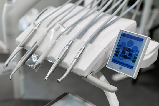 Close-up of modern dental instruments and handpieces mounted on a dental treatment unit with a touchscreen control panel in a clean clinical environment. Shallow depth of field