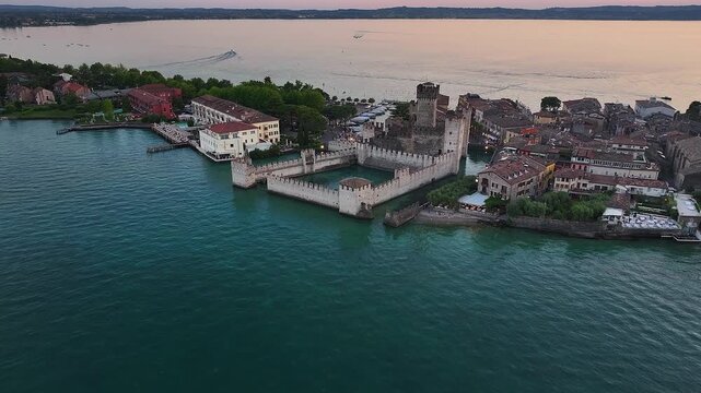 Sirmione, Italy - 4K Flying above Scaligero Castle (Castello Scaligero di Sirmione) at the comune of Sirmione, located at the lower part of Lake Garda. Sunset, dramatic golden sky and clouds