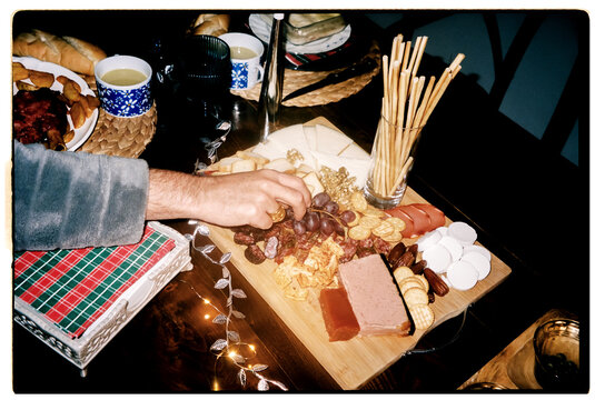 A male hand takes a grape from a festive charcuterie board indoors