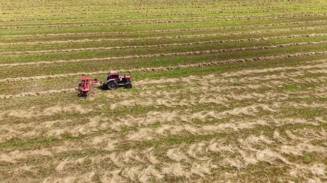 Tractor towing grass mower across harvested field with clear blue skies and vibrant green grass