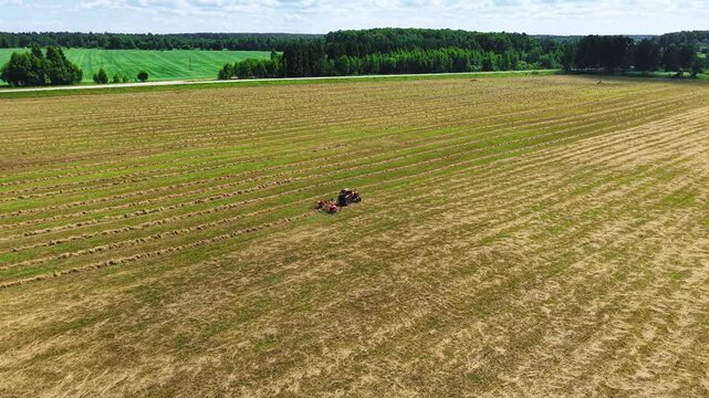 Tractor harvesting grass in a field marked with cut rows under a bright blue sky, aerial view