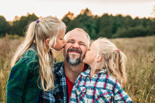 Daughters kiss their smiling father in a grassy summer field