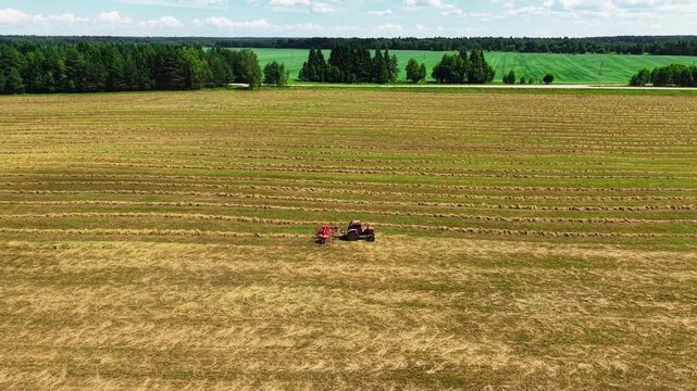 Red tractor harvesting hay in striped green and yellow agricultural fields under a clear sky
