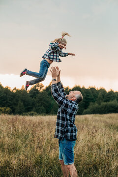 Father throws his happy daughter into the air in a meadow