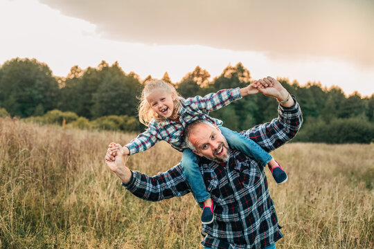 Father carries his laughing daughter in a grassy field