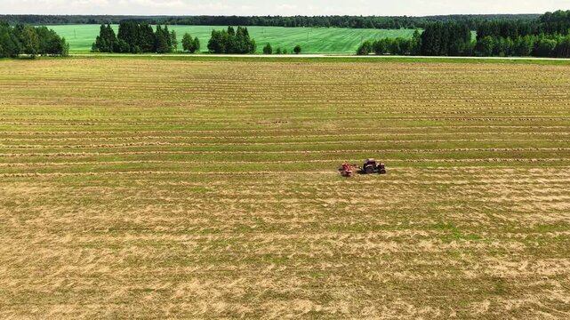 Tractor performing field preparation in large open farmland under clear skies in summer, aerial view
