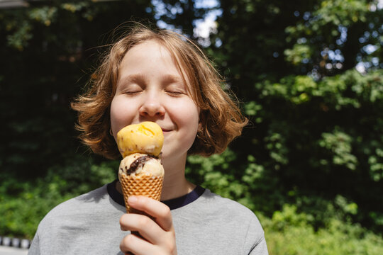 Smiling teenage girl eats sweet ice cream outdoors in summer