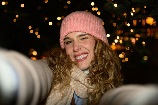 Smiling woman takes a night selfie near an urban Christmas tree