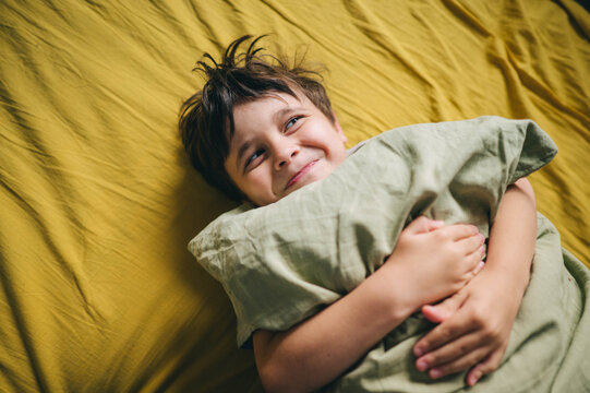 Happy boy hugs a green pillow in bed during the morning