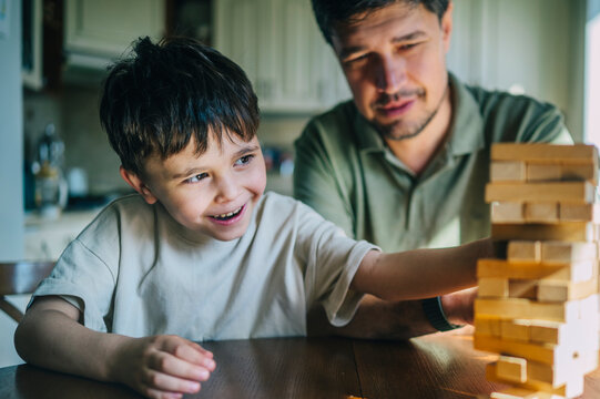Smiling father and son play a wooden block tower game indoors