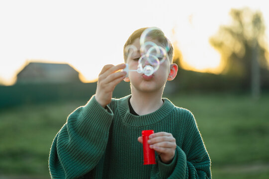 Boy blowing soap bubbles outdoors in summer