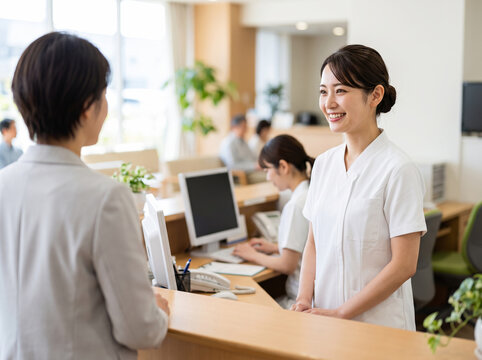 病院の受付窓口で来院した患者に対し丁寧な笑顔で接客する受付スタッフの女性