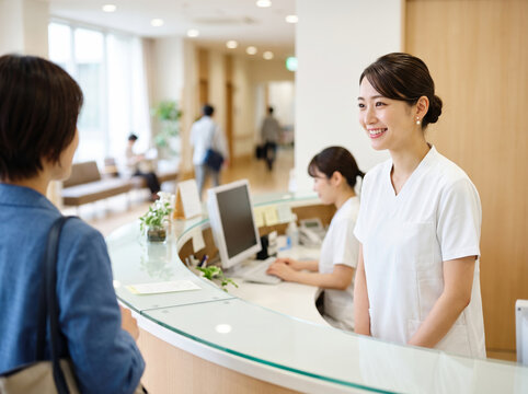 病院のカウンターで来院した患者に明るく対応する受付の女性