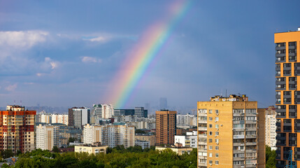Naklejka premium Bright rainbow over city skyline after rain with apartment buildings and blue cloudy sky