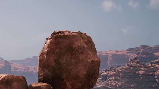 A large rock formation is seen in a desert area. The sun shines on the rocks, highlighting their texture. The sky is clear with few clouds, showing the vastness of the scenery.