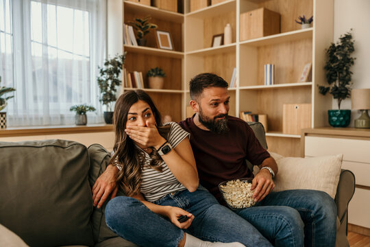 Couple reacting to scary movie with popcorn on sofa