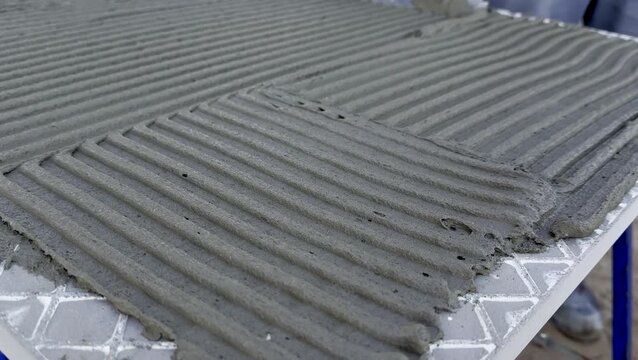 Worker applies cement mixture with a trowel to a surface, creating smooth, textured lines in the concrete, showcasing the progression of the task in a construction setting