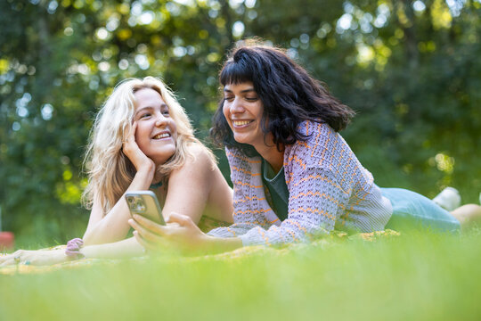 A woman and a friend look at a smartphone in a summer park