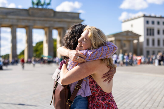 Female friend hugs woman at Brandenburg Gate in Berlin