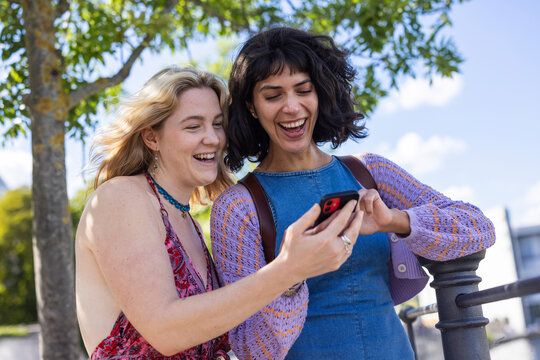 Woman and friend laugh at a smartphone outdoors in Berlin