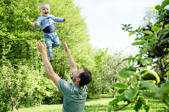 A father throws his baby son into the air in a spring garden