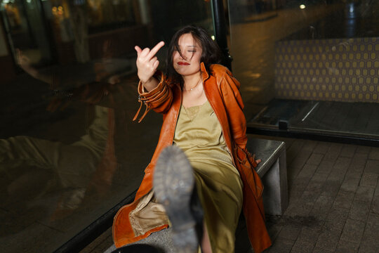 Woman in raincoat showing middle finger at bus stop