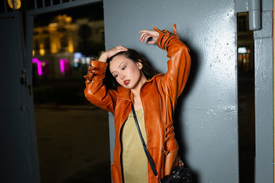 Model posing in a red raincoat by an iron gate in the city at night