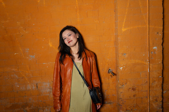 Smiling model in raincoat leaning against brick wall in the city