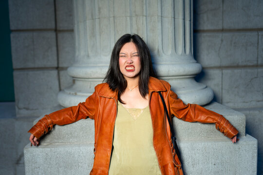Woman grimacing while leaning against a stone building in the city