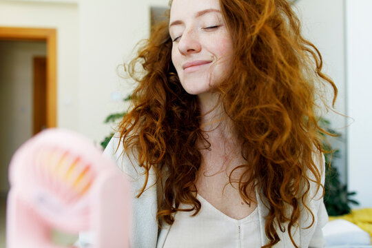 Woman with brown hair holding portable fan at home