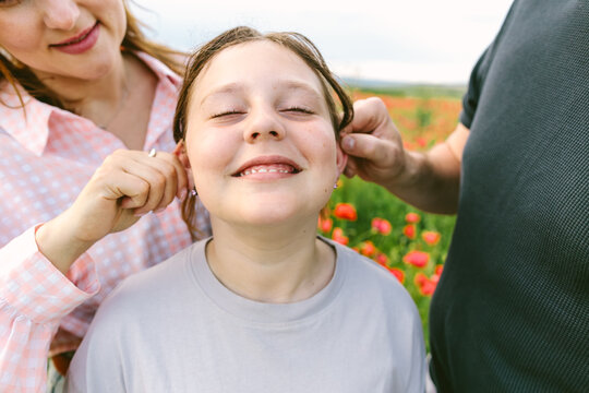 Mother and father playfully pull their smiling daughter's ears