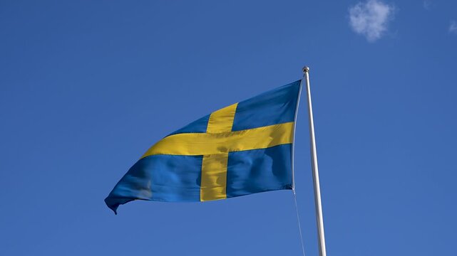 Swedish flag on flagpole against blue sky. Flag of Sweden waving on flagpole in Stockholm. Swedish national flag.