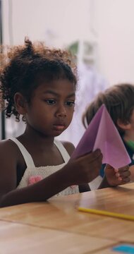 Cute African American little girl playing with colorful paper airplanes in the classroom.