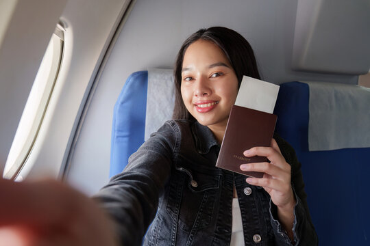 Asian woman taking selfie with passport and boarding pass on airplane