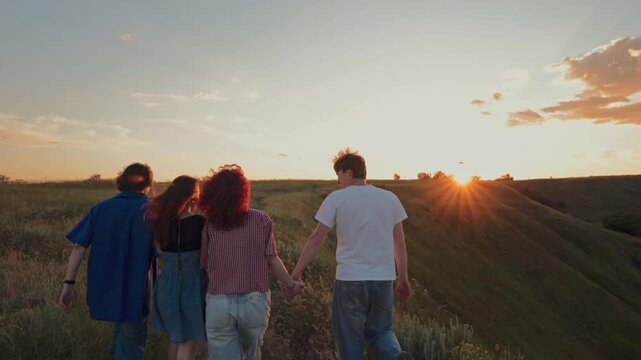 Group of friends walking together through meadow at sunset. Concept of weekend trip, hiking with friends, group travel, social gathering and outdoor recreation.