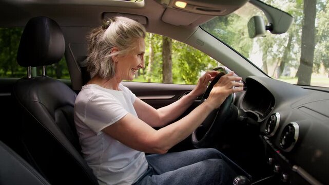 Joyful Caucasian happy old woman using rental service choosing new car for test drive in city smiling sitting inside touching steering wheel retired senior aged female in auto salon choose automobile
