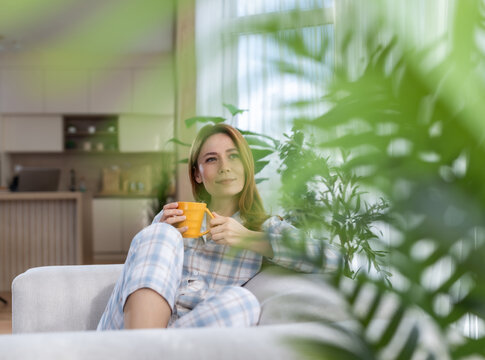 Woman drinks coffee in a cozy room with plants in the morning