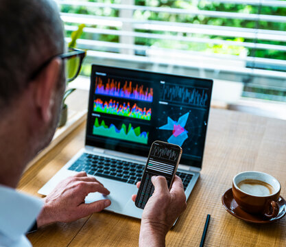 Man analyzing financial data on laptop and mobile in the office