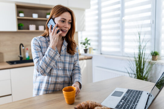 Woman on phone and laptop at kitchen counter