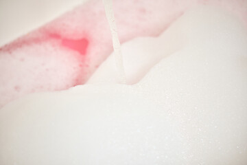 Fototapeta premium Water pouring into a bathtub, creating white foam and pink bubble bath for a relaxing spa and wellness experience