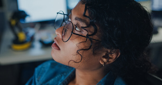 Close-up young Black female programmer coding AI software on multiple screens in night office. Network security, cybersecurity, machine learning, working late, overtime, robotics automation concept.