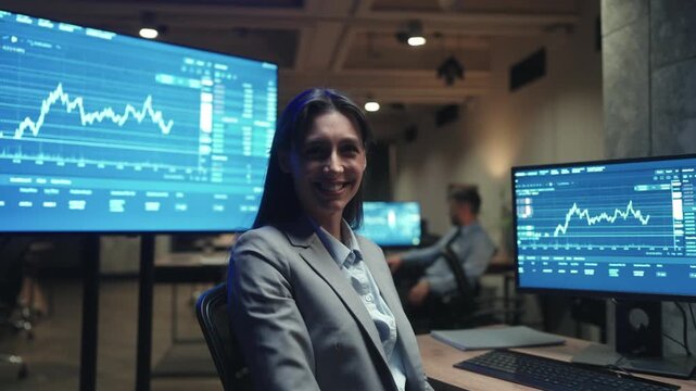 Side view Caucasian female trader using computer and mouse while watching financial charts. Woman broker analyzing stock market data in dark trading office. Professional working late at night.