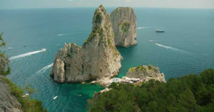 Faraglioni sea stacks rise from deep blue Mediterranean with boats circling in summer and famous beach club da Luigi ai Faraglioni