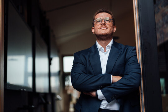 Confident businessman with freckles looks out the office window