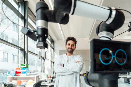 Smiling scientist standing with a robot in a modern laboratory