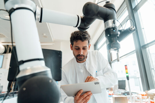 Scientist using digital tablet with robotic arm in laboratory