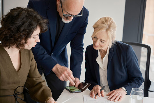 Man shows smartphone to colleague at London office desk