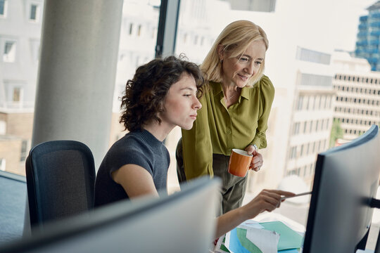 A businesswoman and colleague discuss work at a London office desk