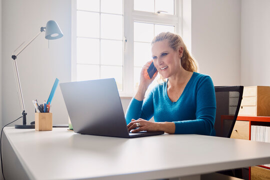A woman works on a laptop computer during a phone call at home