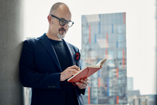 A businessman writes a note in a red notebook at a London office